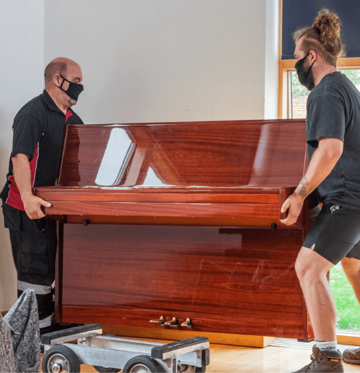 Immagine di due persone che stanno preparando un pianoforte verticale per il trasporto